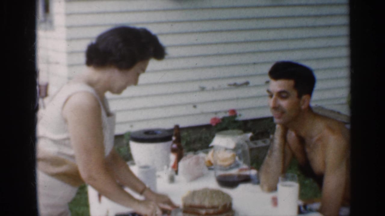 Woman leans over the table near a cake while the man watches from the right.