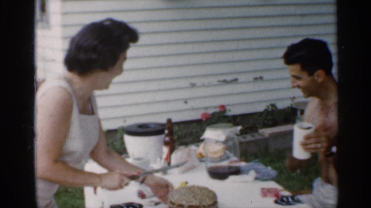 Woman leans over the picnic table as the man smiles and holds a cup.