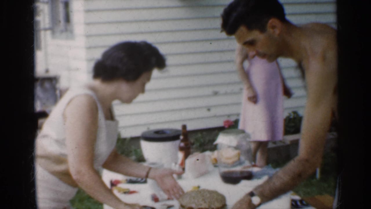 Woman cuts cake while a shirtless man leans over the table and a woman stands behind them.