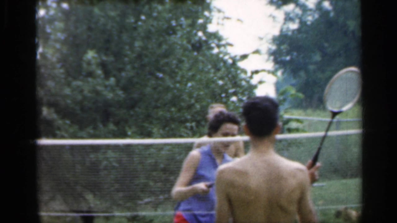 1959 Indiana frame of a shirtless badminton player holding a racket near a woman in a blue top by the net.