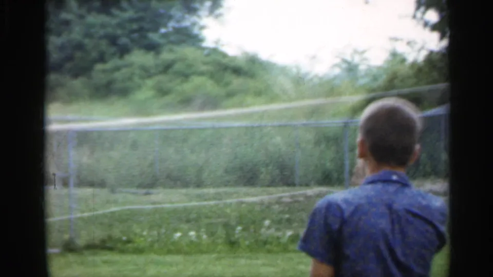1959 Indiana frame showing a badminton player from behind beside the net, with a grassy field and trees in the background.