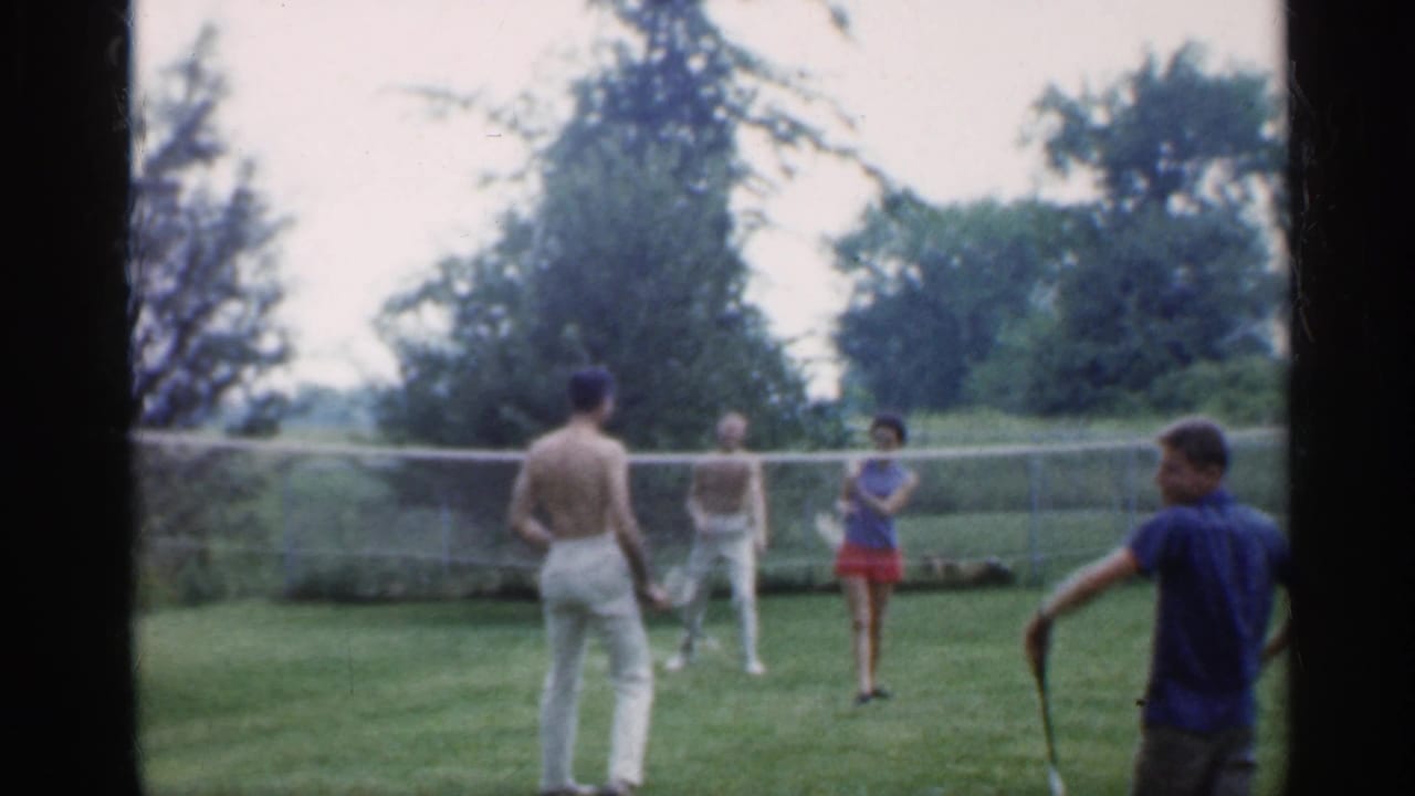 Indiana 1959 8mm frame with adult badminton players on a lawn, including a shirtless man in white pants near the net.