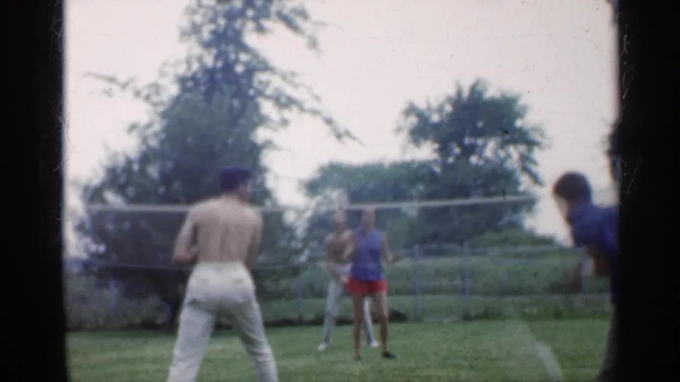 Indiana 1959 8mm frame showing adults in casual summer clothing playing badminton outdoors.