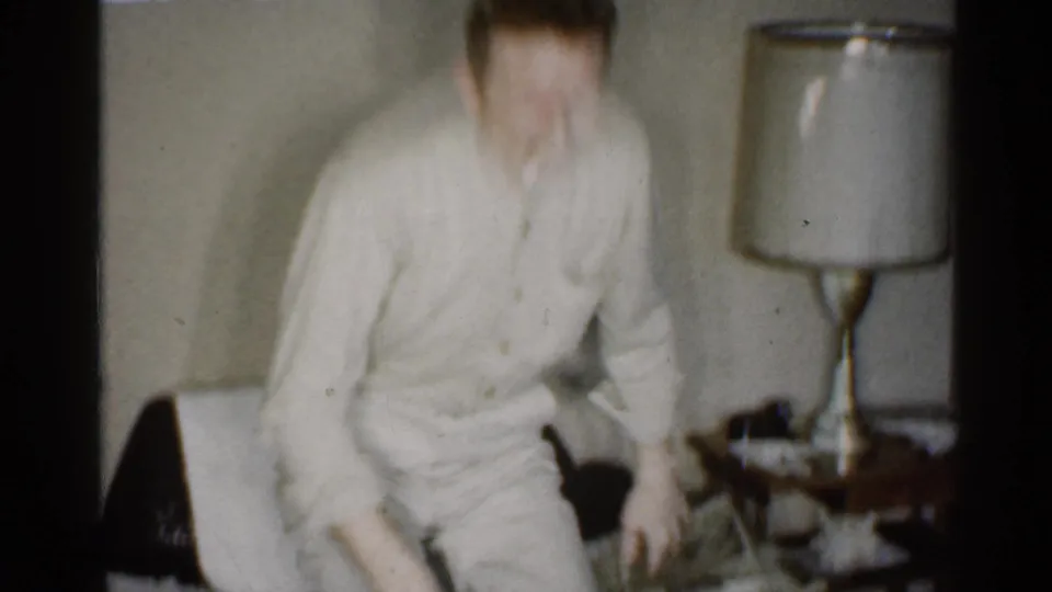The man rises from the armchair, captured with strong home-movie motion blur in the Indiana interior.