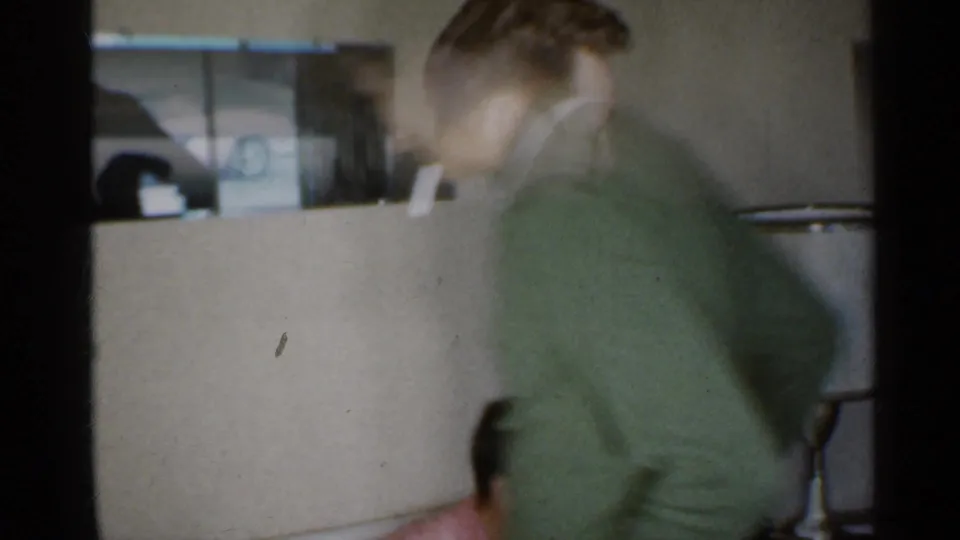 The man moves toward a window in the 1959 Indiana home, with a partial parked car visible outside.