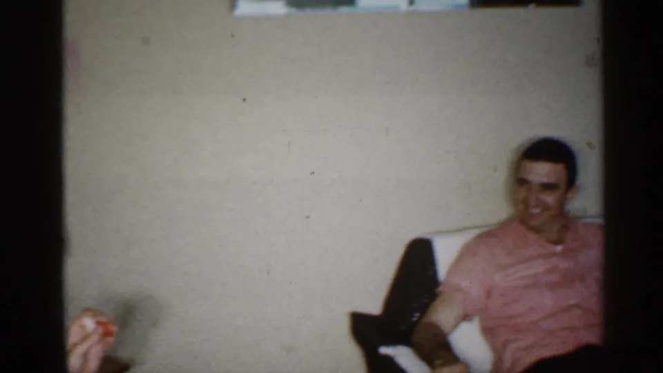 A man in a pink shirt relaxes in the same private living room, seated back in a chair or couch with wall and furniture visible.