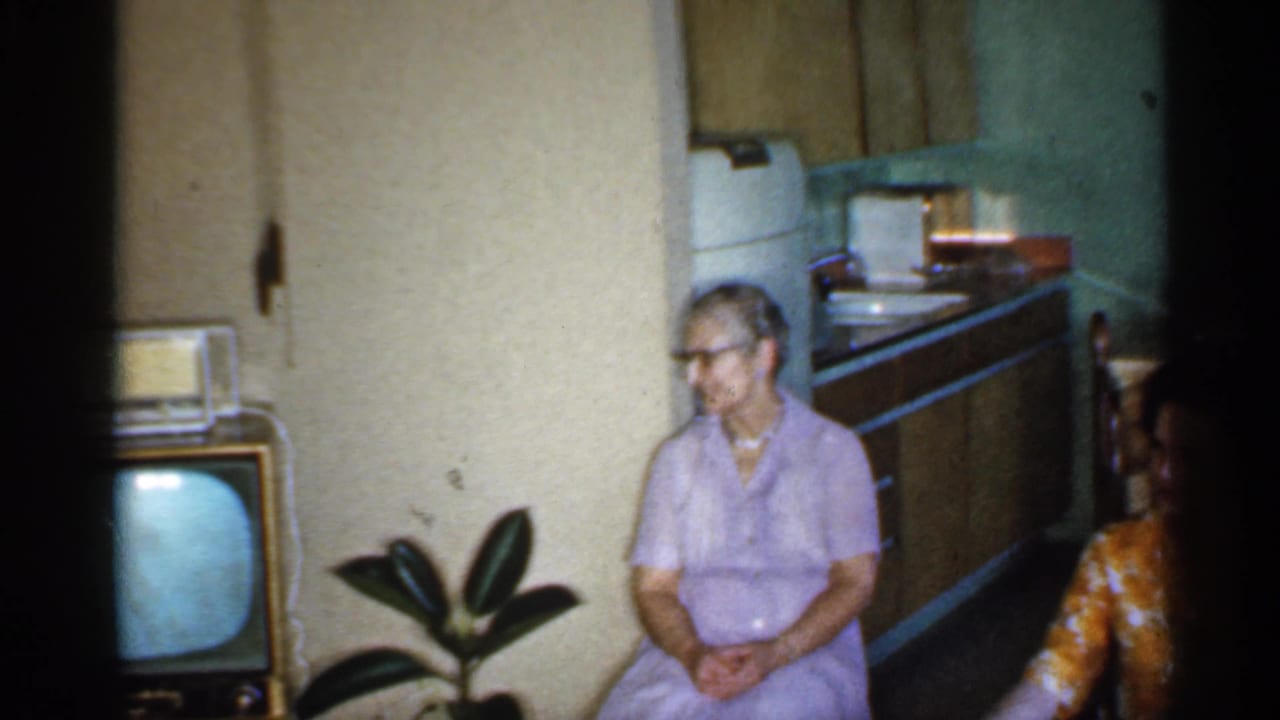 Woman in lavender seated beside a retro television, with part of another seated woman at the edge.