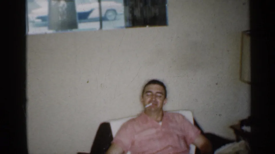 1959 Indiana interior frame of a man seated casually with a cigarette, surrounded by simple household furnishings.