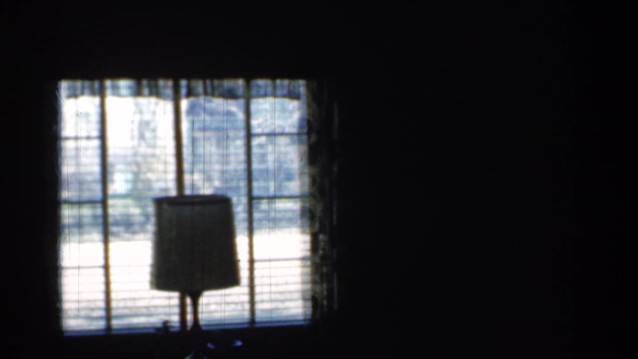 Dark interior with a lamp silhouetted in front of a window with blinds.