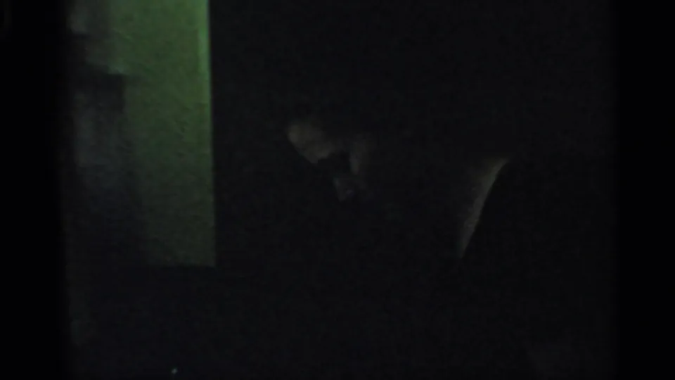 1959 Indiana 8mm frame showing a dim interior with a partially visible person in shadow near a pale vertical wall or doorway.