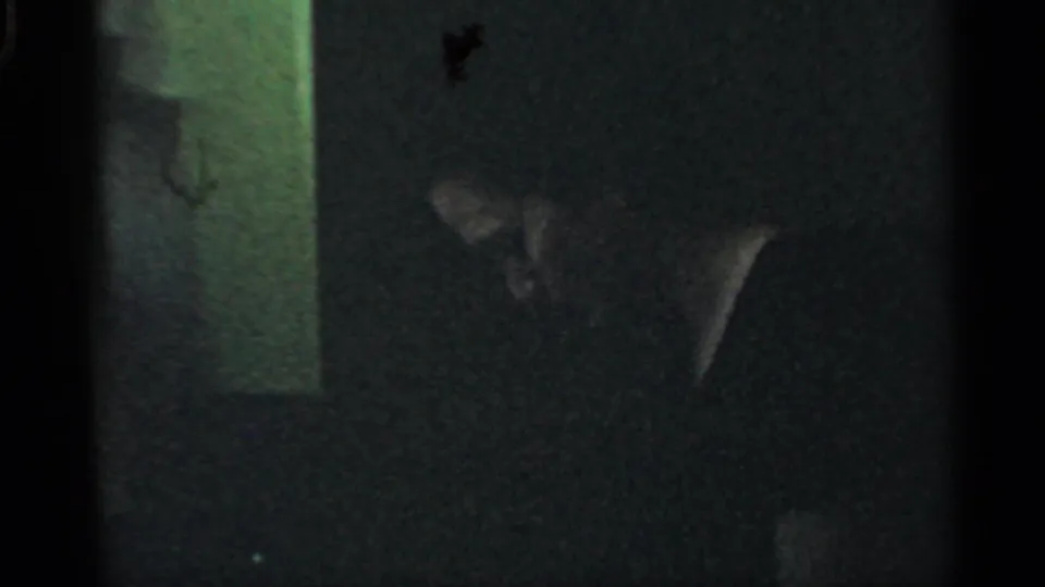 1959 Indiana home-movie frame with a person partly visible in a very dark interior, their face and upper body obscured by shadow.