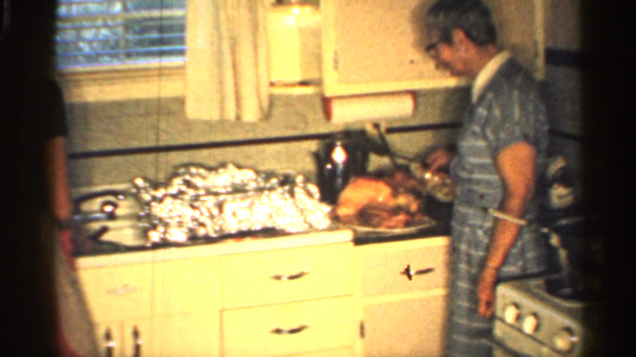 Woman in striped dress carves ham on a kitchen counter beside foil-covered dishes.