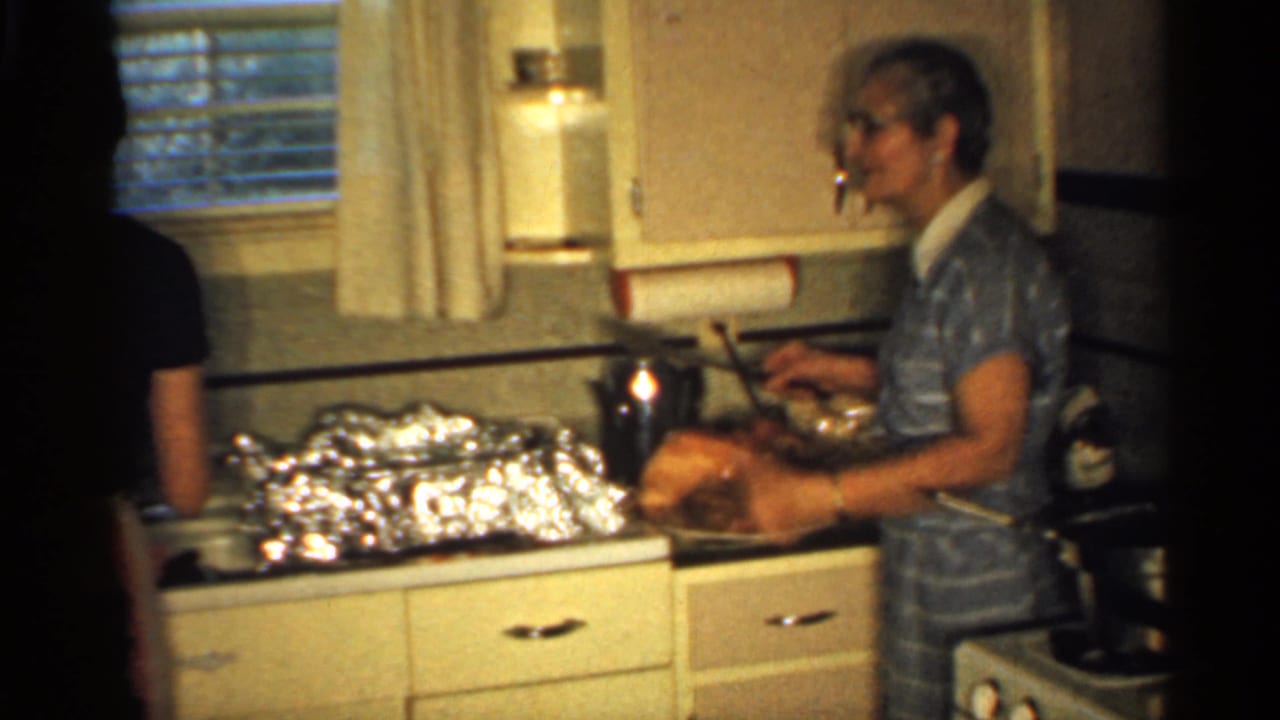 Woman in striped dress works beside a ham, foil dishes, and kitchen stove.