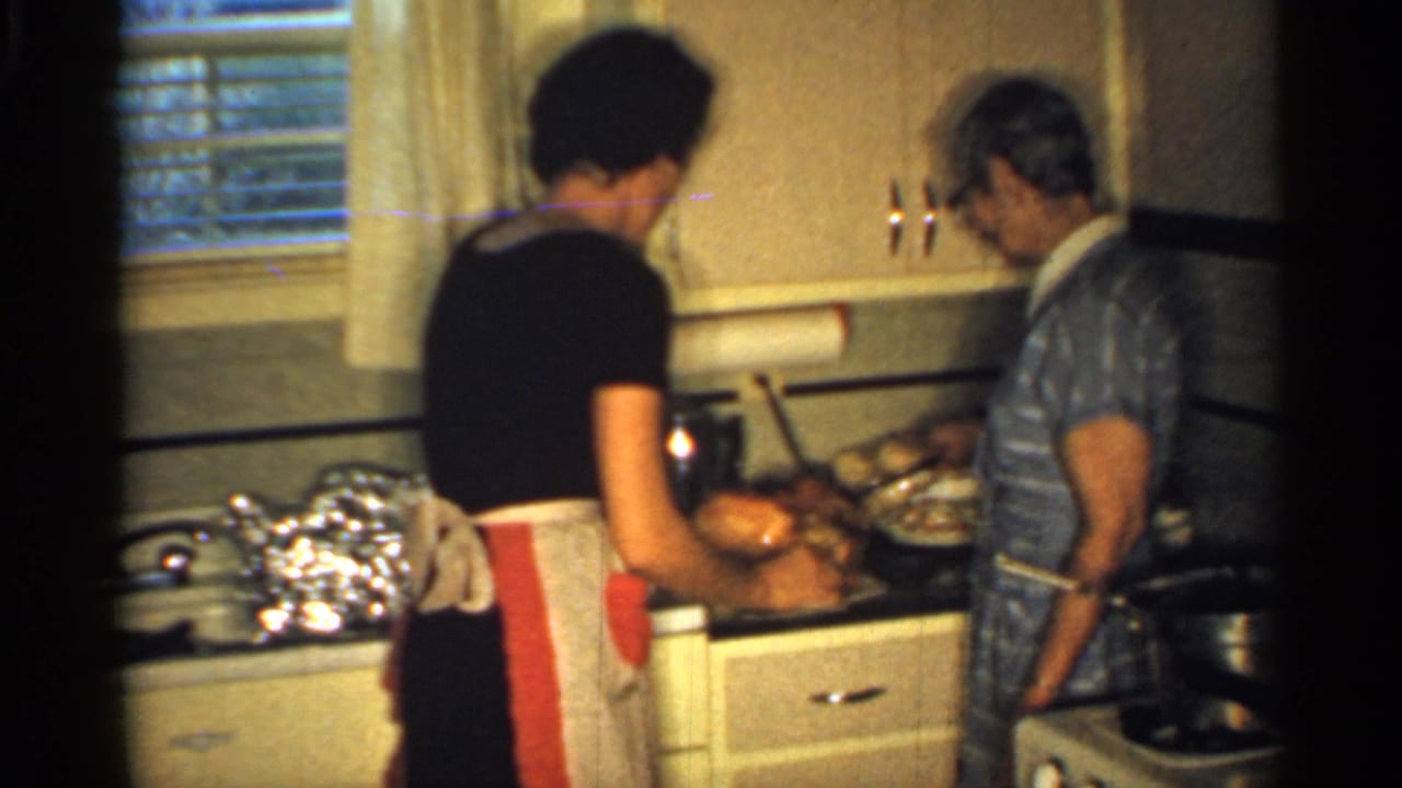 Two women prepare food at a kitchen counter with dishes and foil nearby.