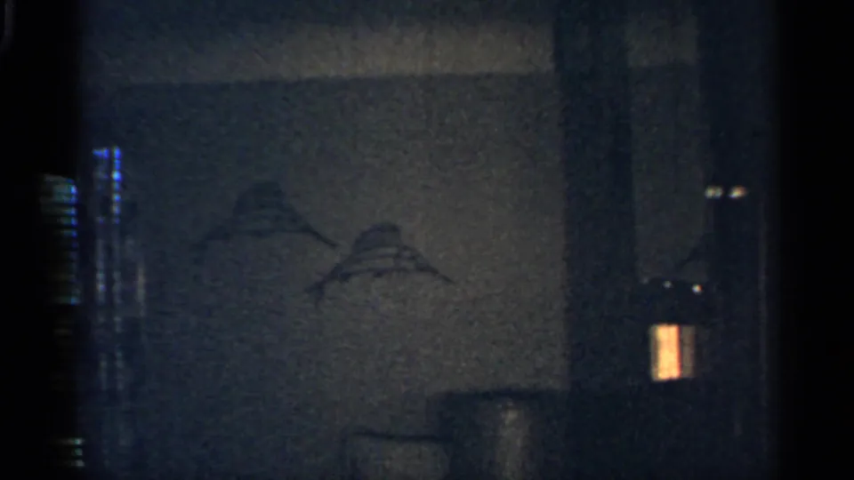 Low-light 1959 Indiana interior detail showing a dark wall, faint wall marks, and a small warm light near the edge.