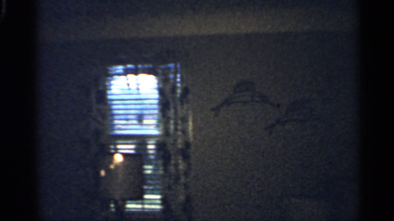 Dim room with bright blinds and wall decoration beside a doorway.