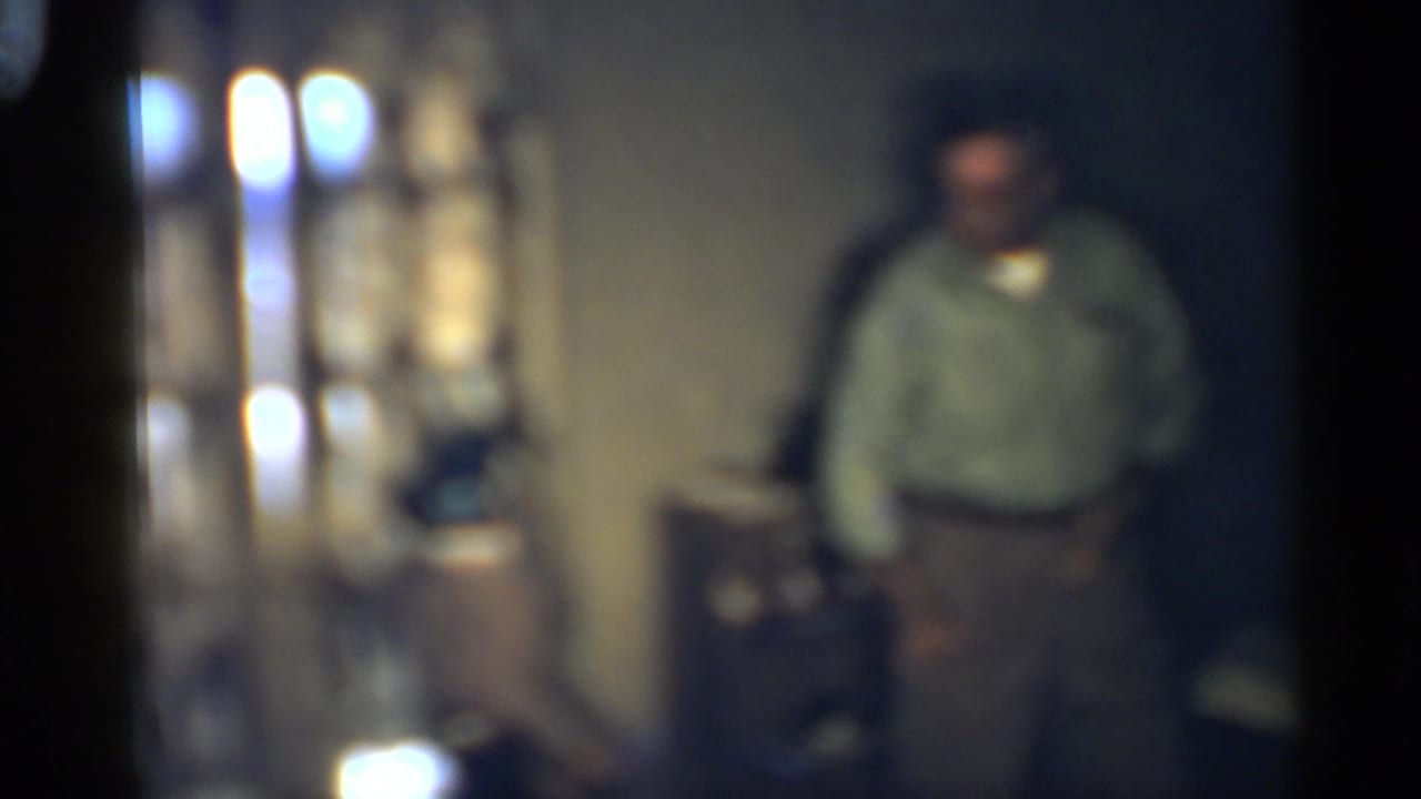 Soft-focused man standing in a dim interior room.