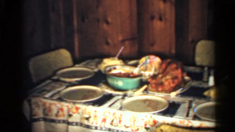 A prepared dinner table in a wood-paneled Indiana interior shows plates, serving bowls, and a roasted turkey on an 8mm home-movie frame.