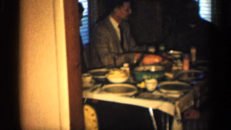 Adult men sit around a dining table in a dim private Indiana home interior, consistent with 1959 home-movie footage.