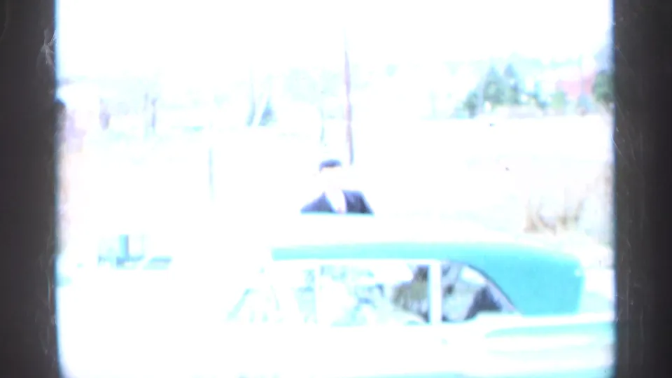 Overexposed home-movie frame showing a man near a green-and-white car outside, supported by the 1959 Indiana clip metadata.