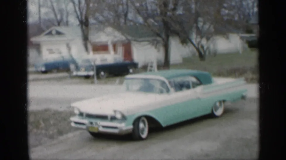 The two-tone convertible is shown from farther back on a quiet Indiana residential road, with a small house and parked car behind it.