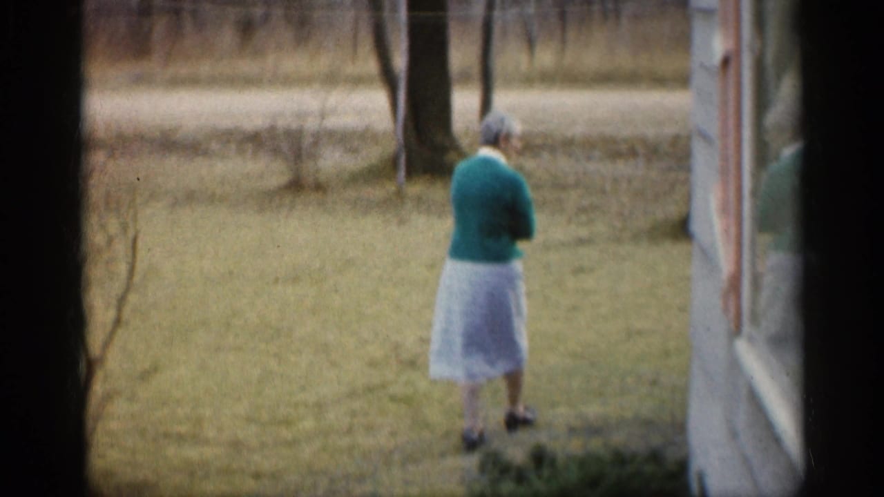 Woman seen from behind walking near a house window across a grassy yard.