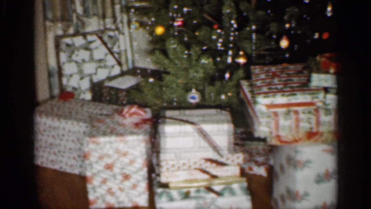 1959 Indiana 8mm frame showing patterned wrapped gifts stacked under a decorated Christmas tree in a family interior.