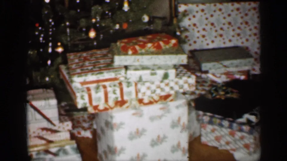 1959 Indiana home-movie frame with large floral, striped, and polka-dot gift boxes beside a decorated Christmas tree.