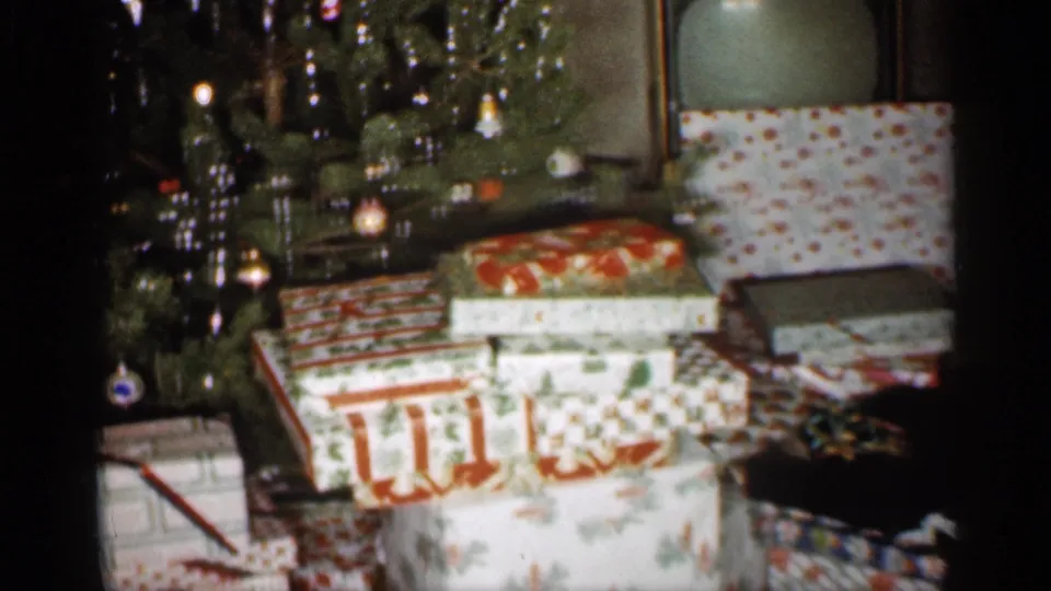 1959 Indiana home-movie frame with ornaments, tinsel, and multiple wrapped Christmas gifts arranged below the tree.