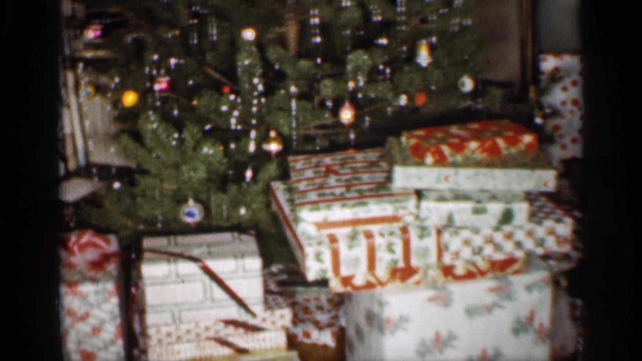 Lit Christmas tree with wrapped presents beneath it in a living room.