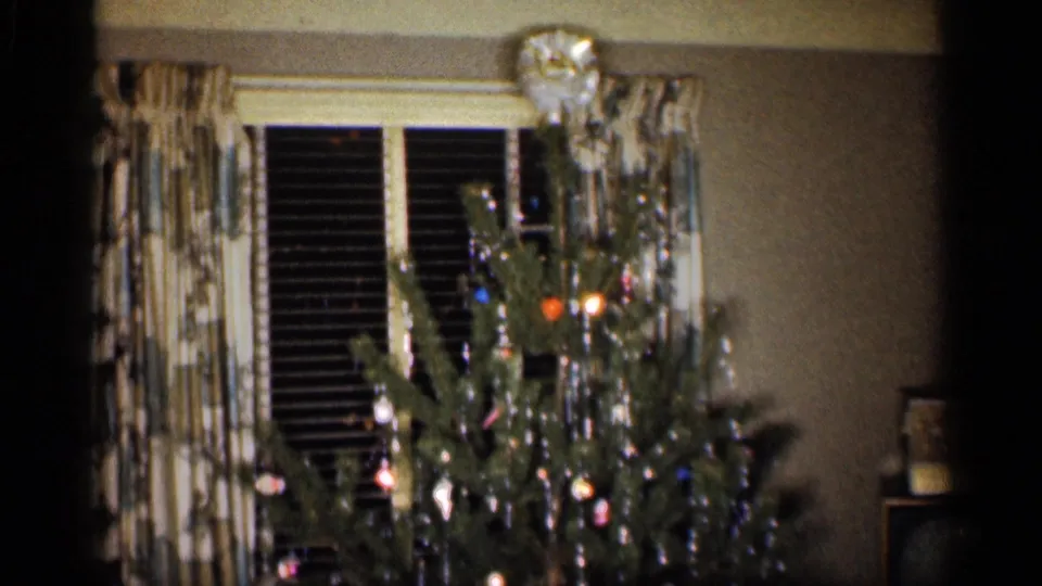 1959 Indiana home-movie frame of a decorated Christmas tree near patterned curtains, window blinds and a small television at right.