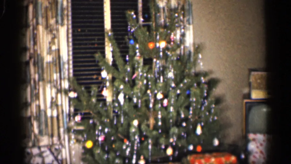 1959 Indiana 8mm frame showing a tinsel-covered Christmas tree filling the foreground with curtains, blinds and television in the room.