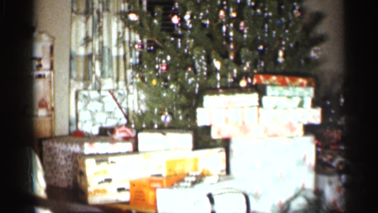 Christmas tree with tinsel and stacked wrapped presents in a living room.