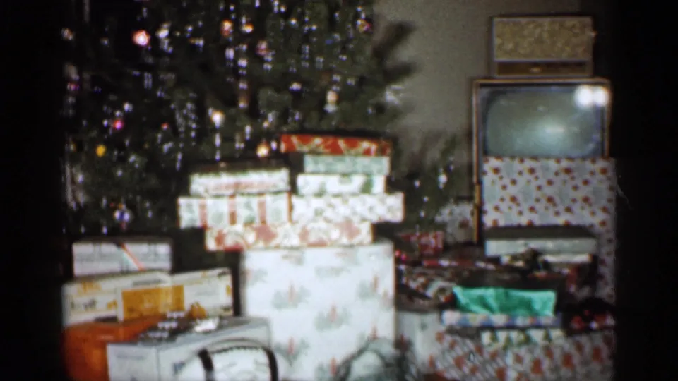 The frame shows wrapped Christmas gifts, a decorated tree, and a television inside a private Indiana living room in 1959.