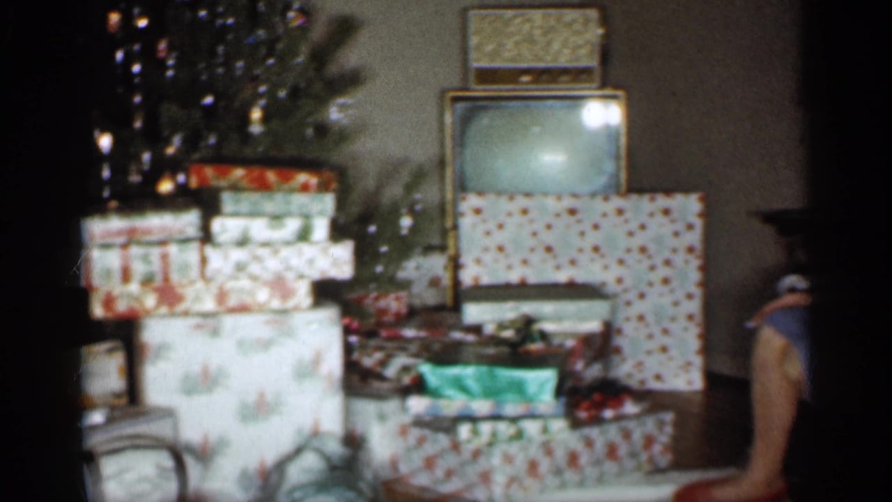 1959 Indiana home-movie frame showing a Christmas tree, stacked presents, a boxy television, and a radio in a private living room.