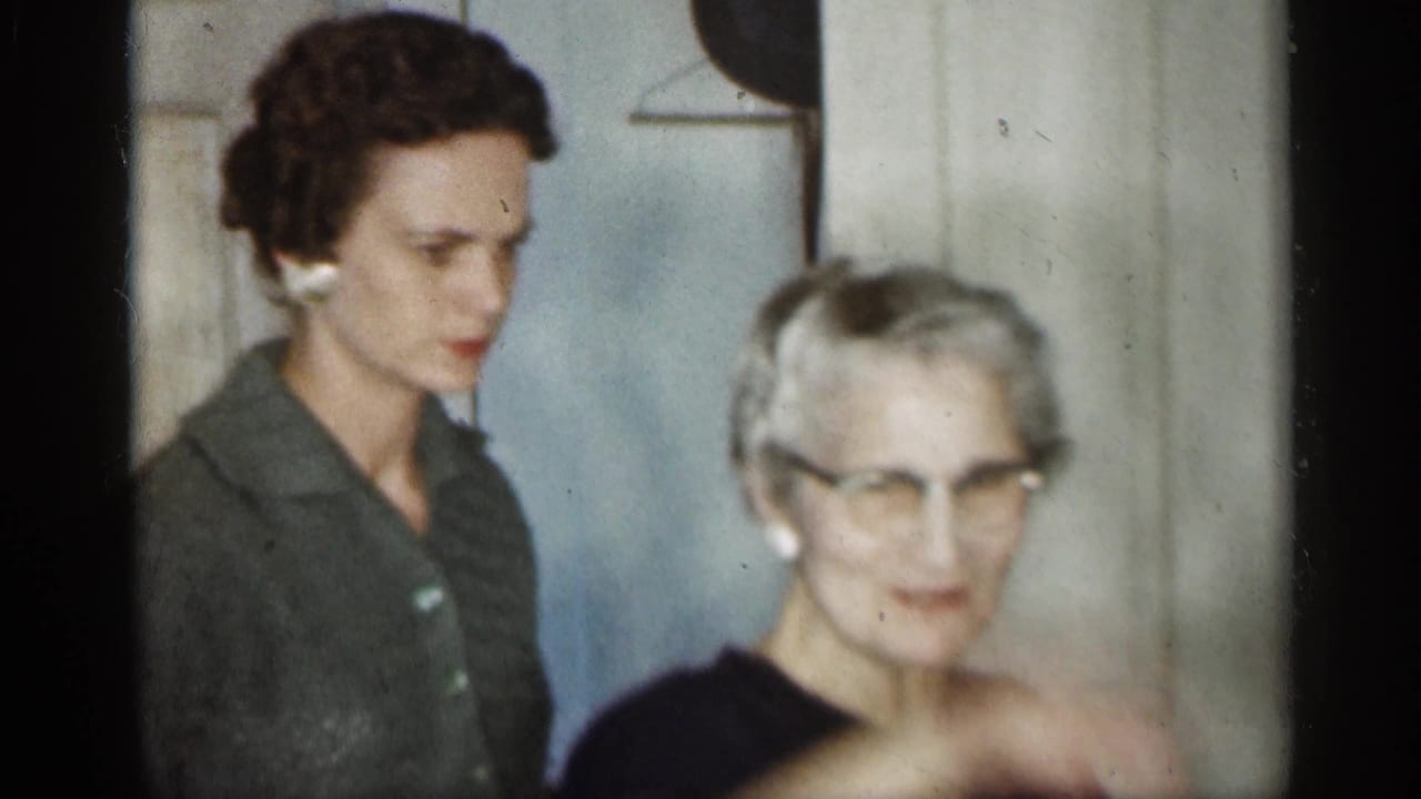 1959 Indiana home-movie frame with an older woman in glasses near a younger woman, both inside a private home.