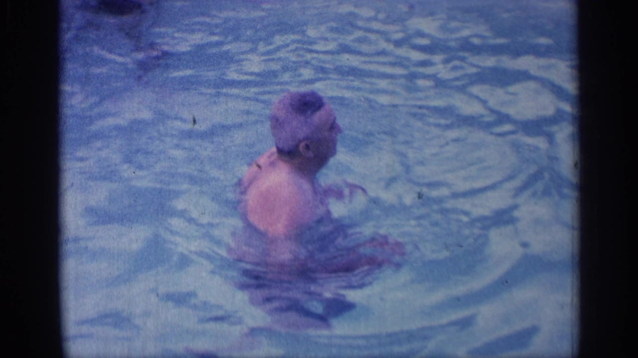 The man turns in the pool during the 1959 Indiana 8mm home movie, surrounded by rippling blue water and soft film grain.