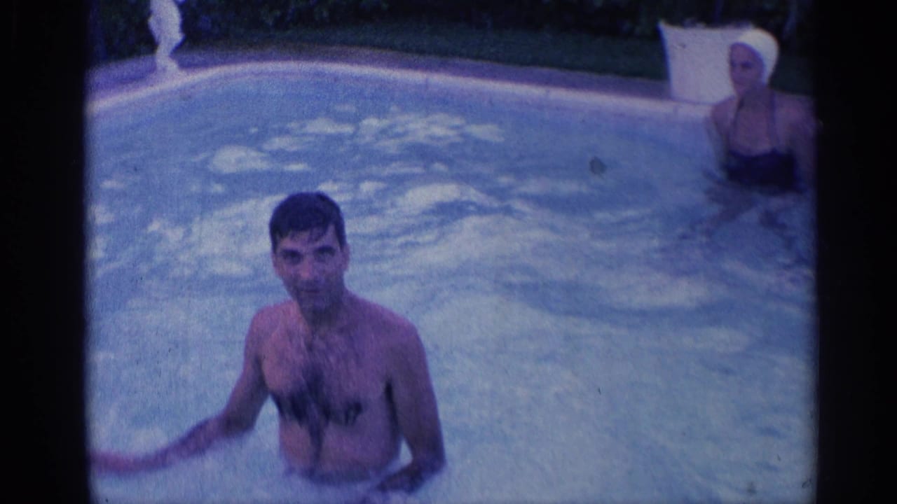 Man standing in a swimming pool with another adult near the pool edge.