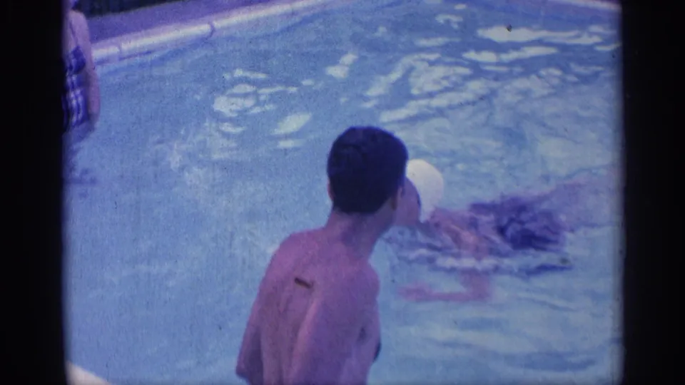A man is seen from behind in the backyard pool as another swim-capped adult moves through the water in the 1959 Indiana footage.