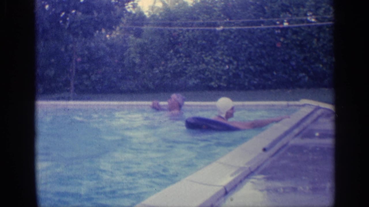 Swimmers in a backyard pool with white swim cap and inflatable ring near the waterline.