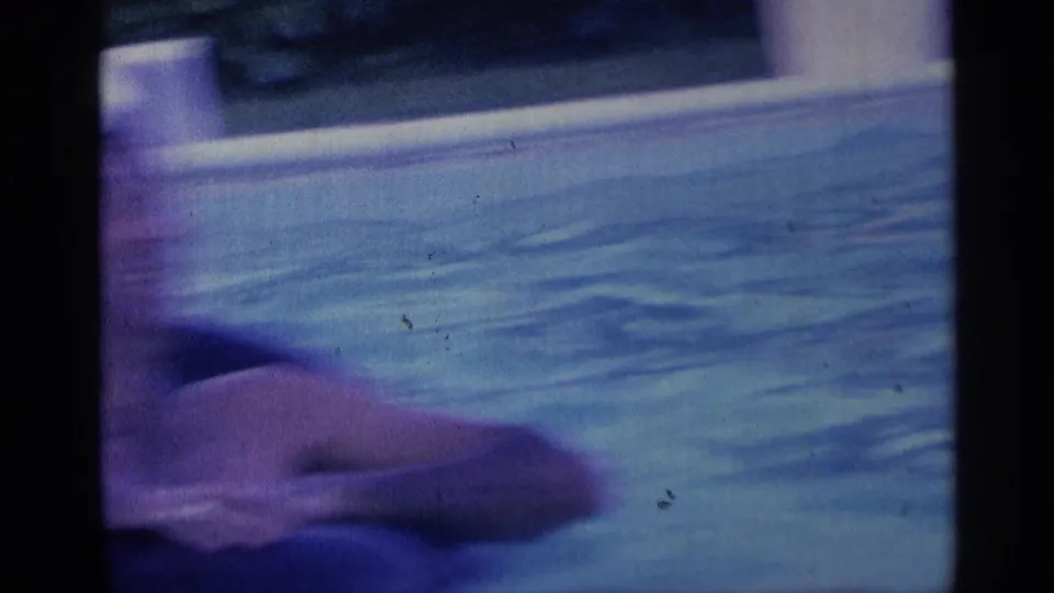 Soft, handheld 8mm frame from the 1959 Indiana pool scene, with water, pool edge, and a partial swimmer close to the camera.