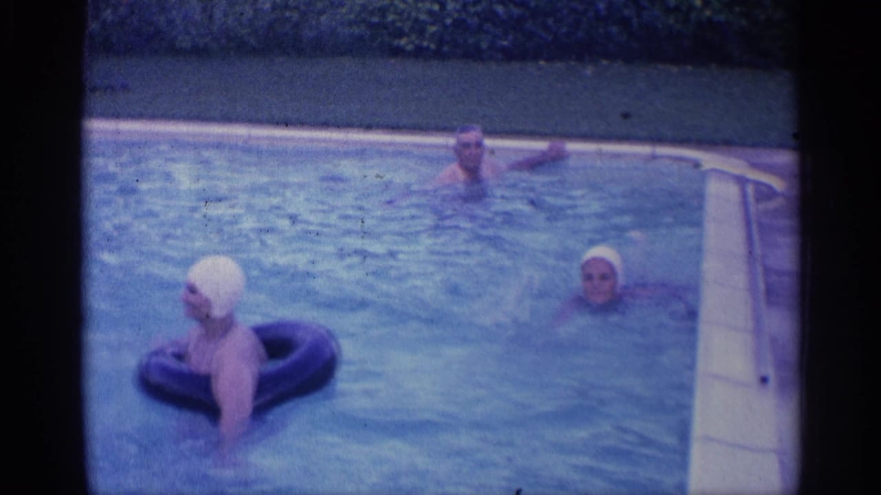 Woman in a white swim cap floats on a black ring while two swimmers are nearby in a pool.