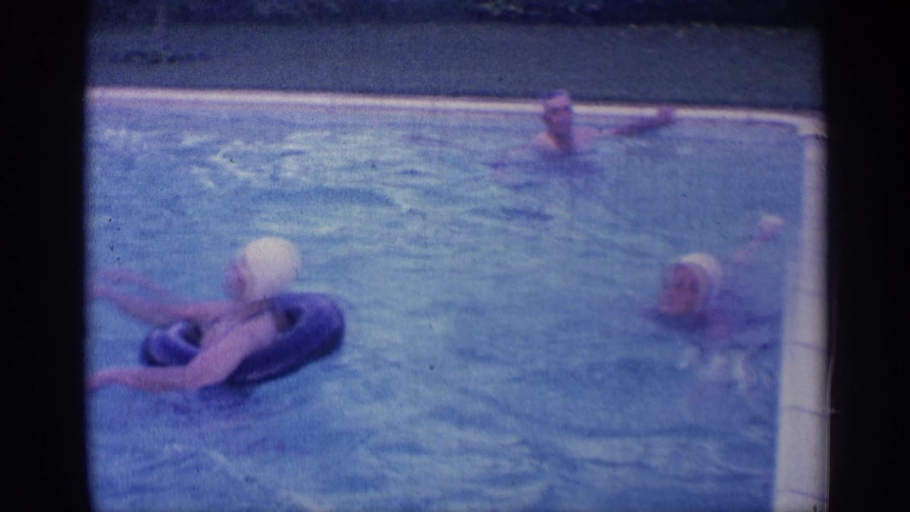 Woman on a black inflatable ring extends her arms as two swimmers remain in the pool.