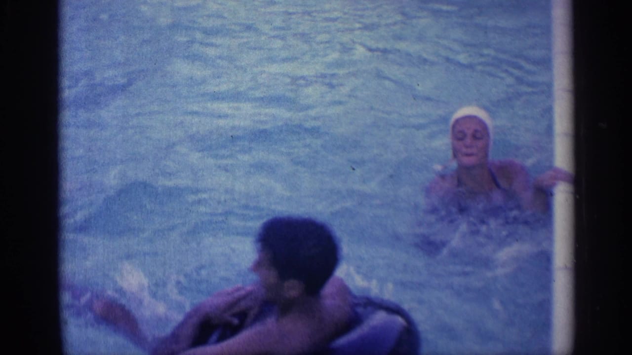 Adults swimming in a pool, with a man near an inner tube and a woman in a white swim cap.