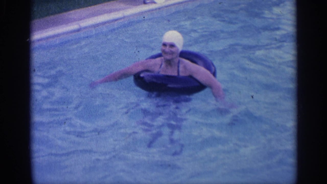 Woman in a white swim cap floats in a backyard pool on a black inner tube.