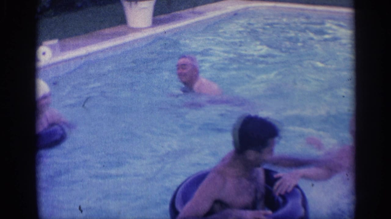 Adults in a backyard swimming pool, one using a dark inflatable ring.