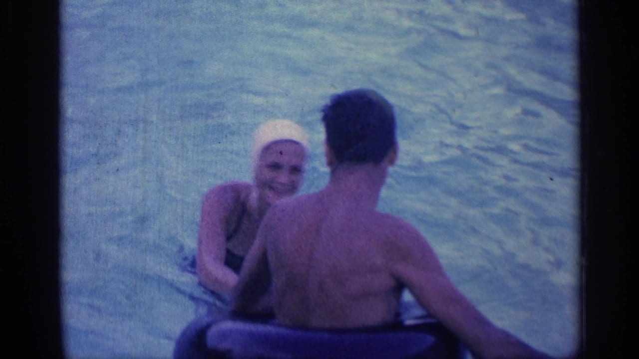 1959 Indiana frame of a woman in a white swim cap smiling toward a man in a backyard swimming pool.
