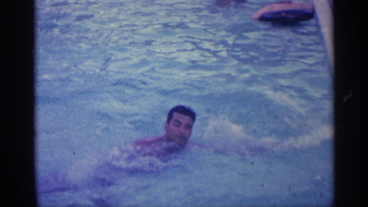 Man in pool facing camera while swimming, with a float or pool object near the top edge.