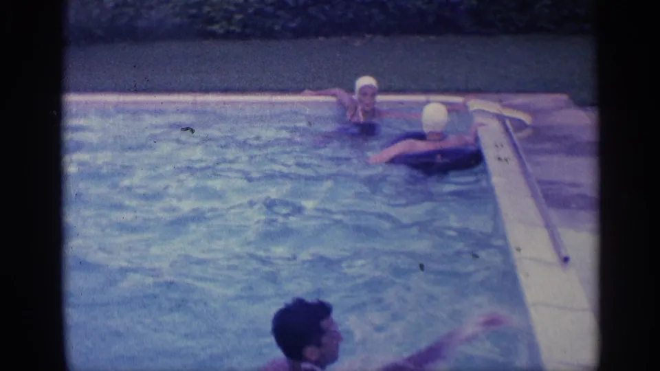 Swimmers gather near the pool edge, including white swim caps, while a man enters the lower foreground in the 1959 Indiana home movie.