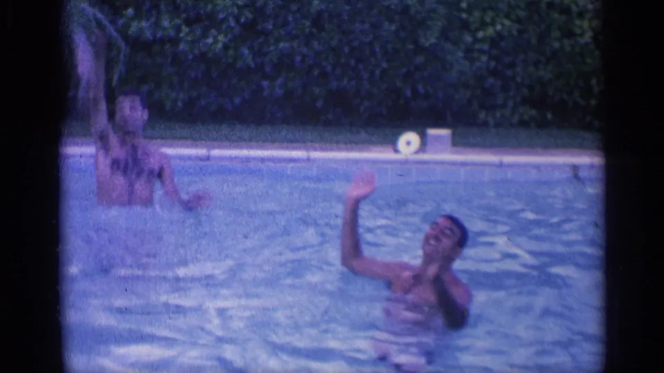1959 Indiana home-movie frame of swimmers in a pool, with one person raising an arm toward the camera.